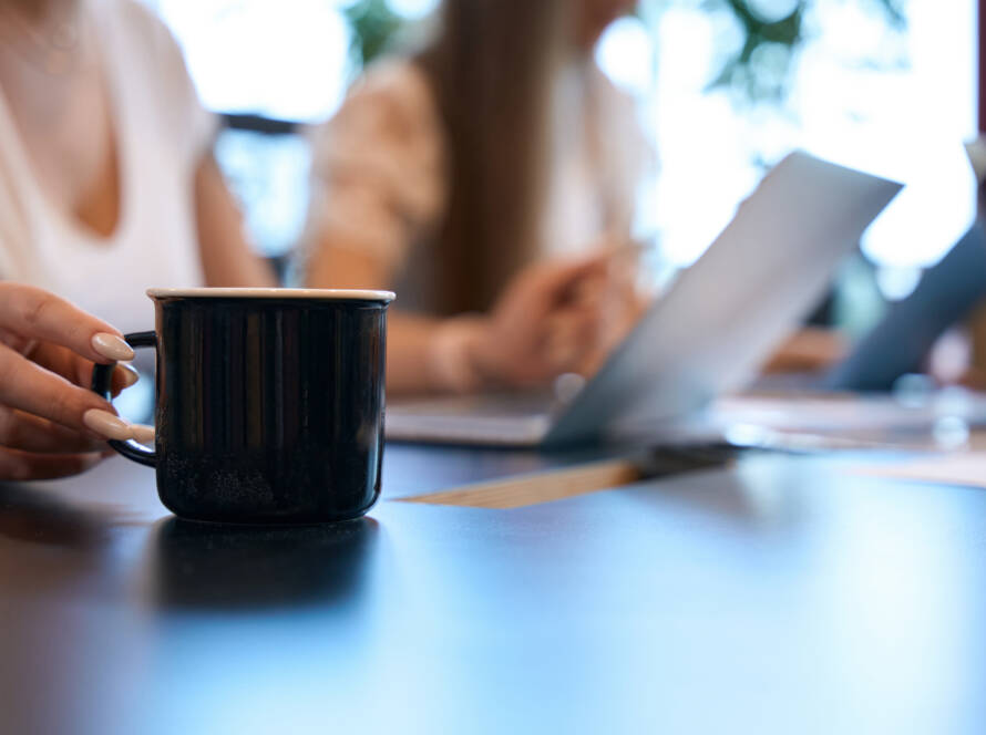 woman reaching for a cup of coffee while in a meeting.