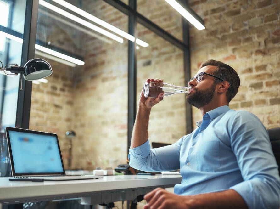 man drinking water in front of his office computer