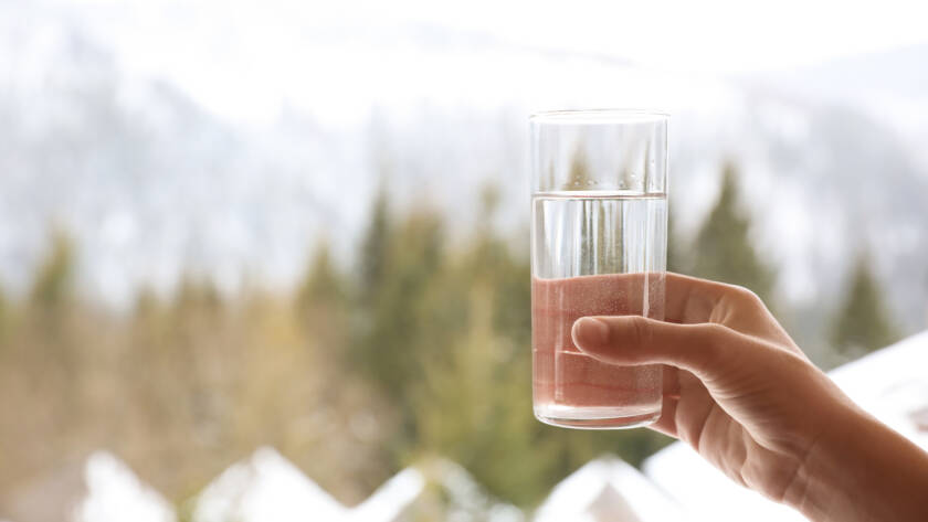 hand holding a glass of water with a winterscape in the background.