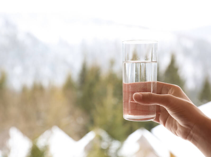 hand holding a glass of water with a winterscape in the background.